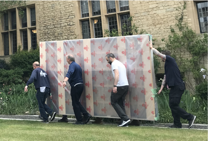 Art technicians carrying the painting across the garden 